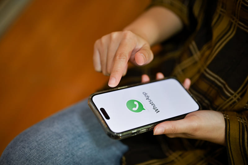 Persona utilizando la aplicación de mensajería WhatsApp en un smartphone para comunicación digital e interacción con clientes en línea Hiweb