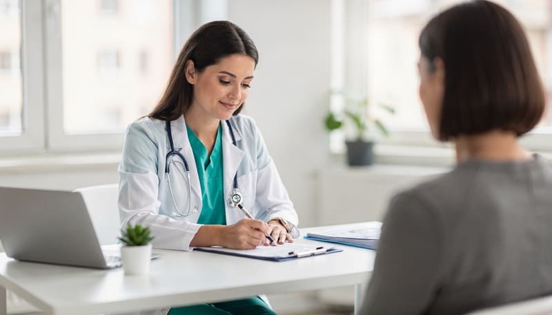 Doctor atendiendo a un paciente en un consultorio médico mientras revisa información y documentación de salud Hiweb