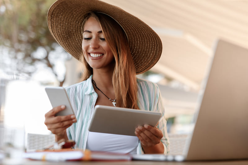 Viajera utilizando smartphone y tablet mientras planea un viaje, representando herramientas digitales para marketing turístico Hiweb