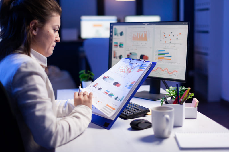 Analista de negocios revisando reportes de datos y gráficos de rendimiento en una computadora Hiweb