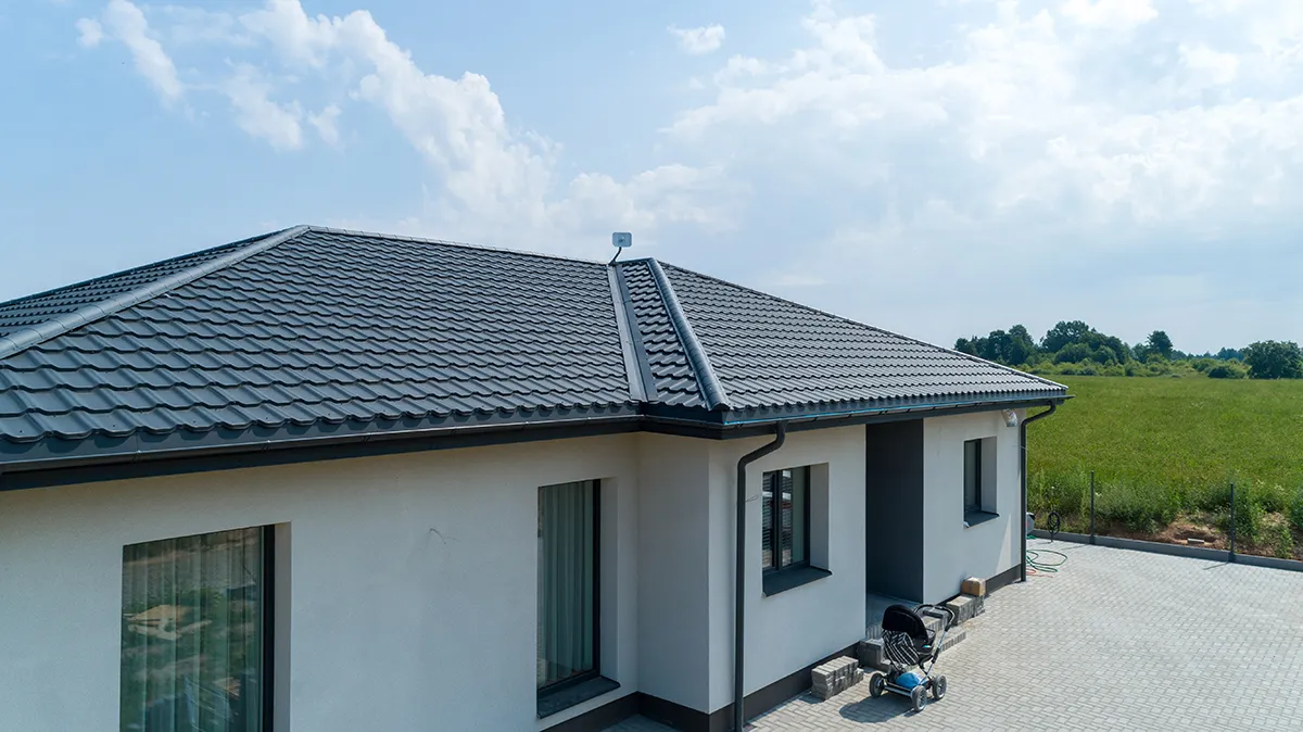 Modern egyszintes ház sötétszürke cseréptetővel, zöld rét mellett.