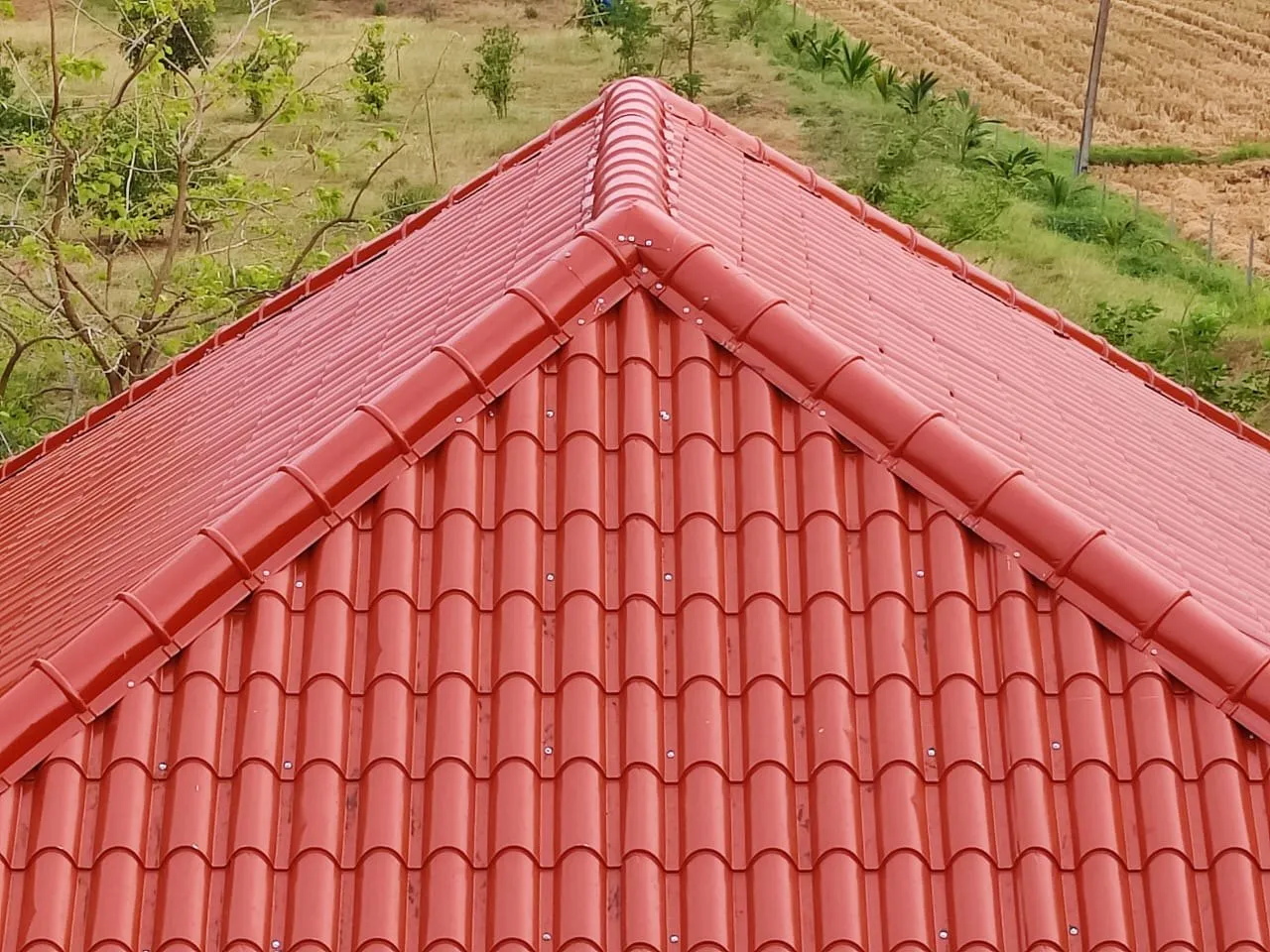 Piros cseréptető háromszög alakú részlete zöld kert háttérrel.