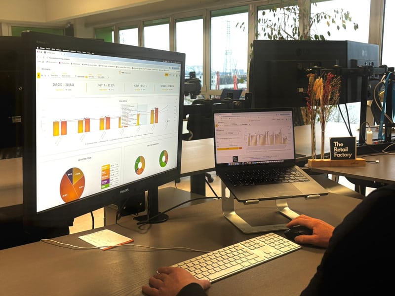 Personne travaillant à un bureau avec un ordinateur portable et un grand écran affichant des tableaux et des graphiques, avec des fenêtres de bureau en arrière-plan.