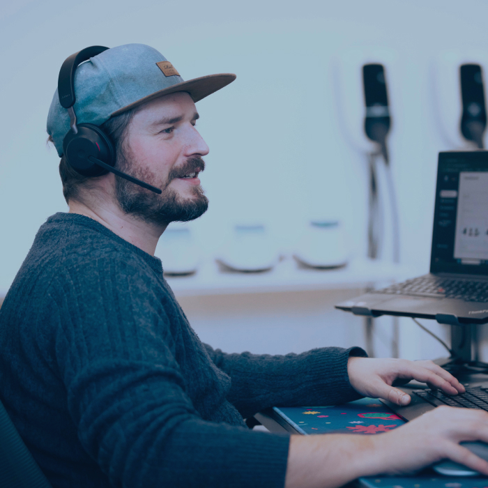 ChargeX Support Mitarbeiter mit Headset vor einem Laptop und dem Aqueduct Ladesystem im Hintergrund