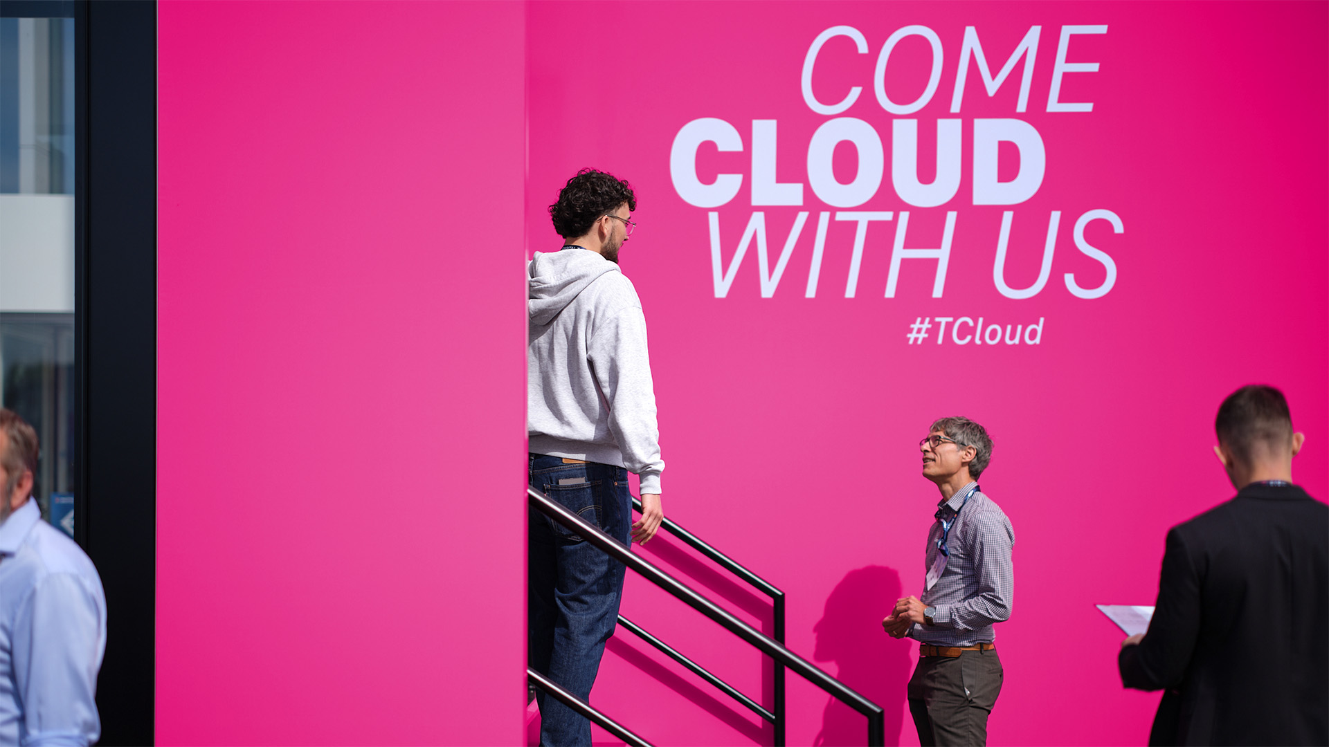 Besuchende betreten die T Cloud von T‑Systems über einen Zugang mit leuchtenden Elementen und Spiegelwänden.