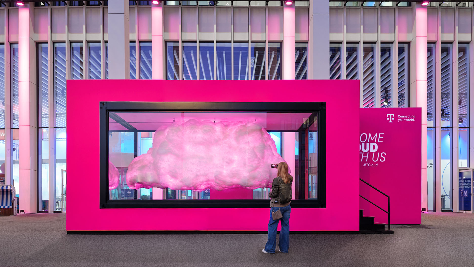 Abendstimmung an der T Cloud von T‑Systems mit leuchtenden Datenpunkten und Besucherinnen und Besuchern auf der Plaza.