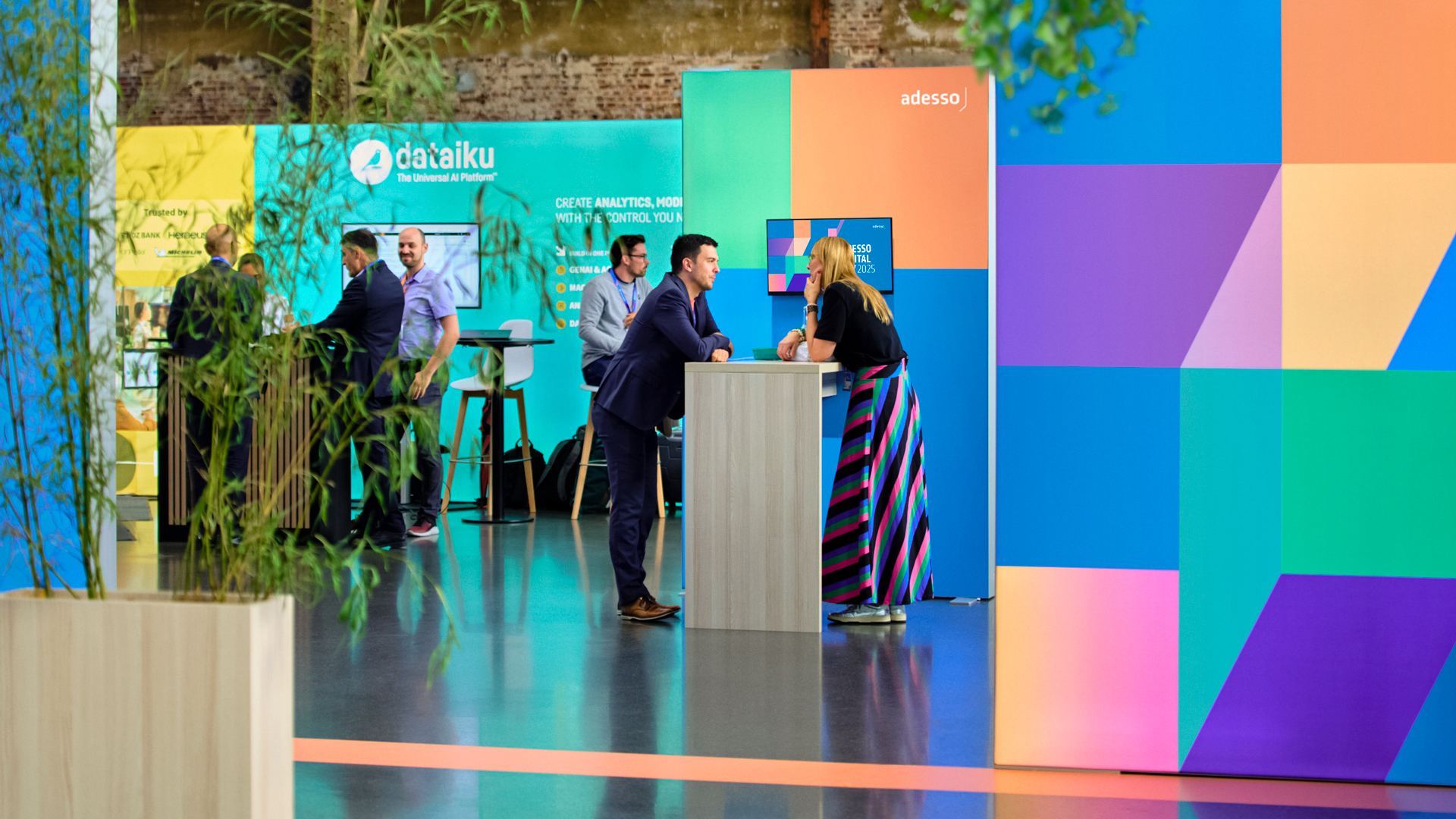 Networking-Bereich beim Adesso Digital Day 2025: Teilnehmende im Gespräch vor farbigen Messewänden im Adesso-Eventdesign von Phocus Brand Contact.