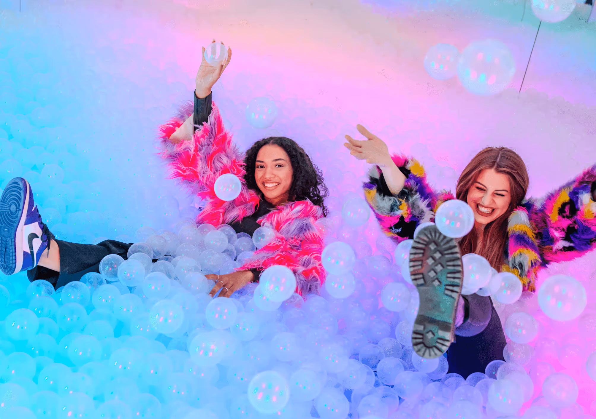 two girls in colorful clothes having fun in a ballpit.