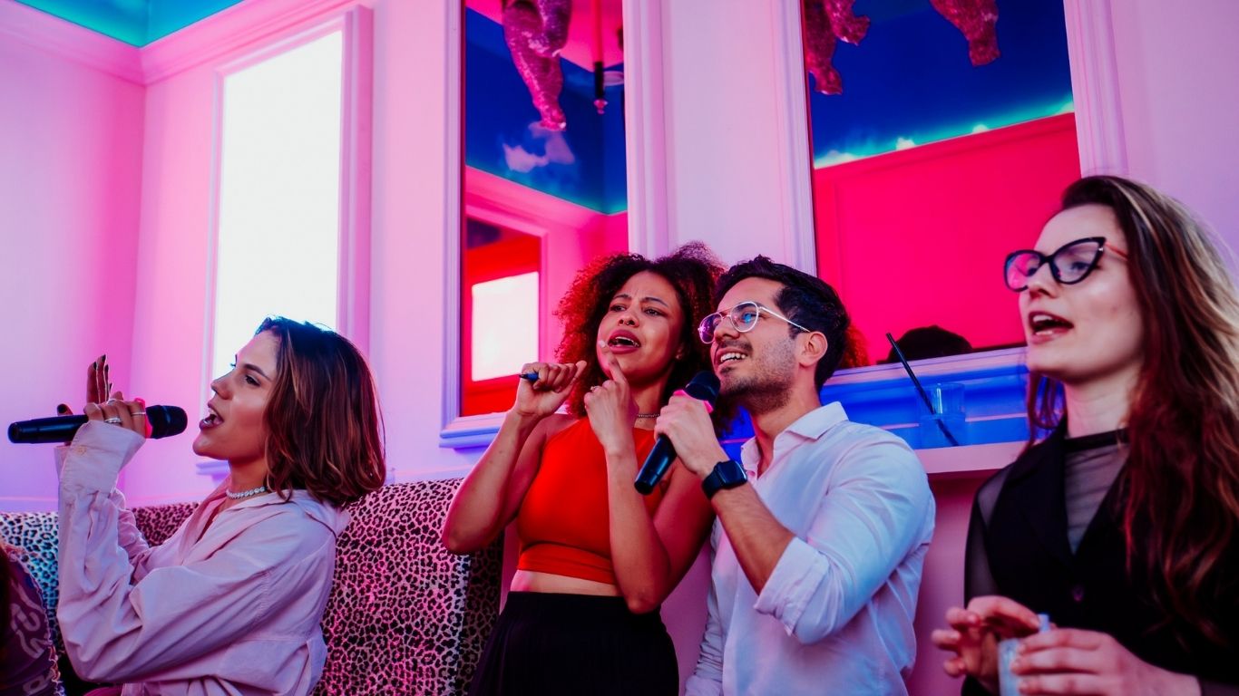 Group of people singing into a microphone in a pink karaoke room.