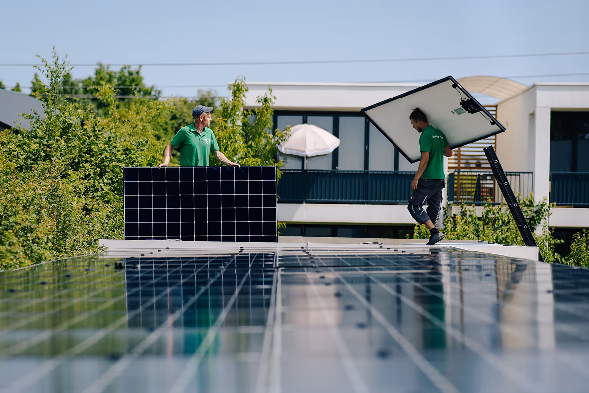 Twee monteurs verwijderen zonnepanelen van een plat dak tijdens een renovatie, met professionele uitrusting en veiligheidsmaatregelen, op een zonnige dag bij een modern gebouw.