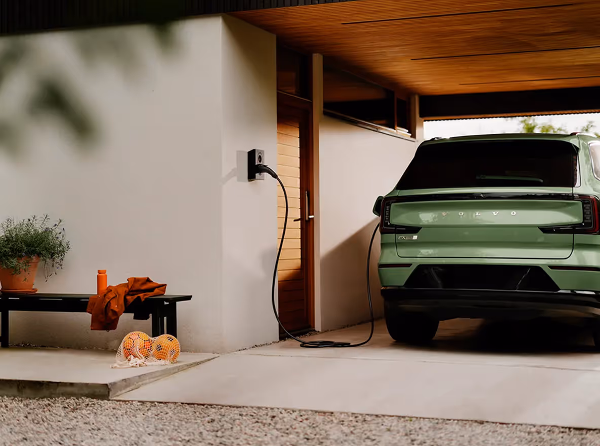 Elektrische auto wordt opgeladen bij een houten woning met open kofferbak en bagage klaar voor vertrek.