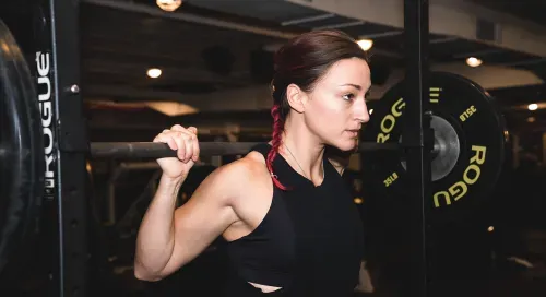 Woman doing squats at squat rack in new york city. Body building gym Completebody.