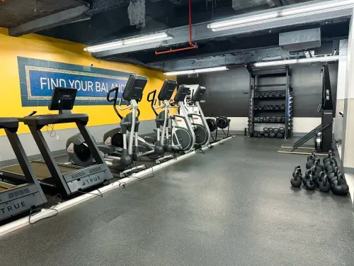 Gym with treadmills, ellipticals, kettlebells, rowing machines, and black wall with equipment rack.