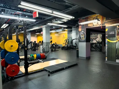 Spacious gym interior with weightlifting platforms, colorful weight plates, and various exercise machines.