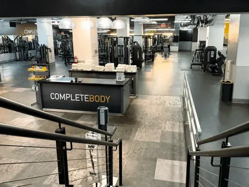 Modern gym entrance with CompleteBody desk, stacked towels, and various workout machines inside.