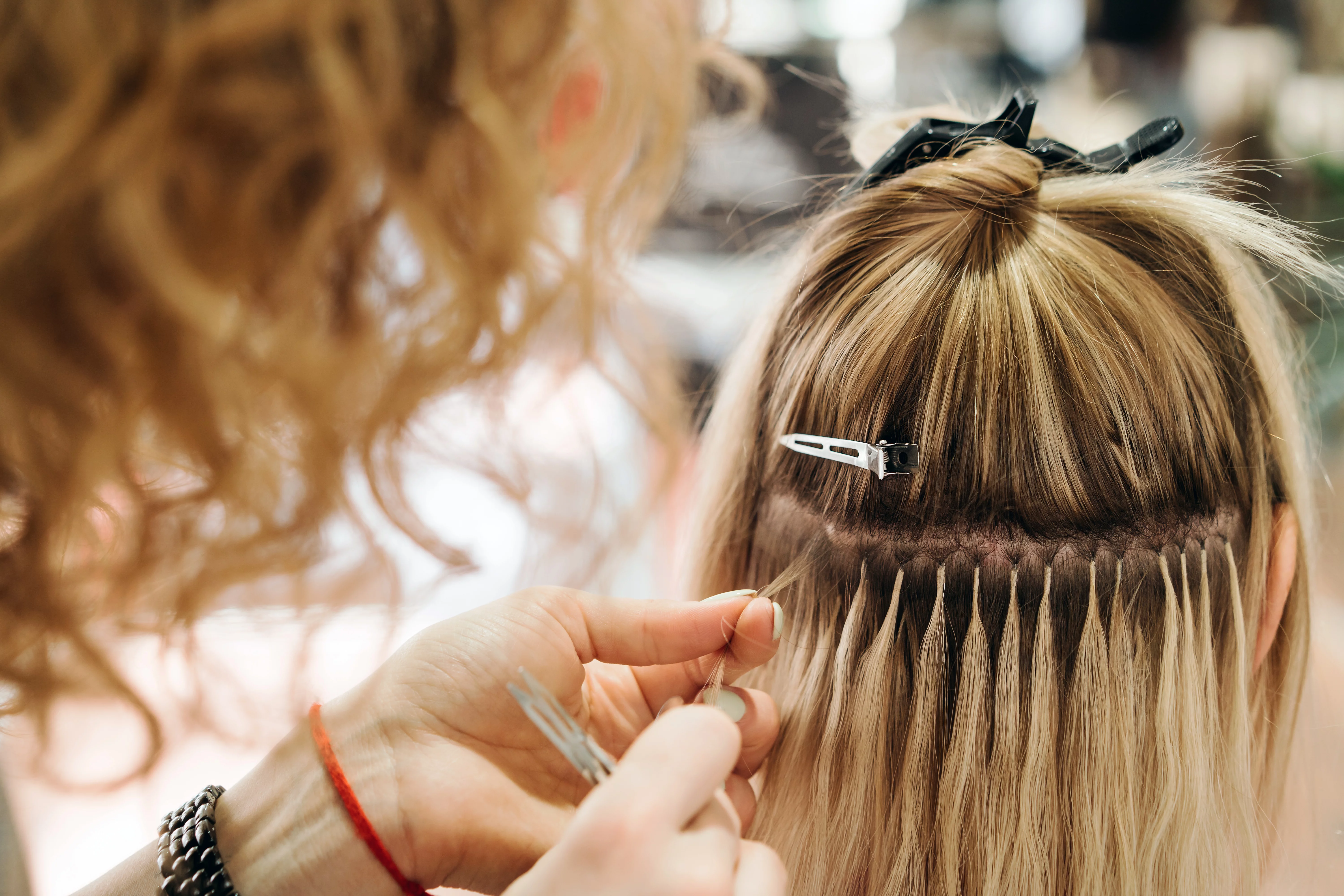 Woman placing hair extensions on blonde hair 