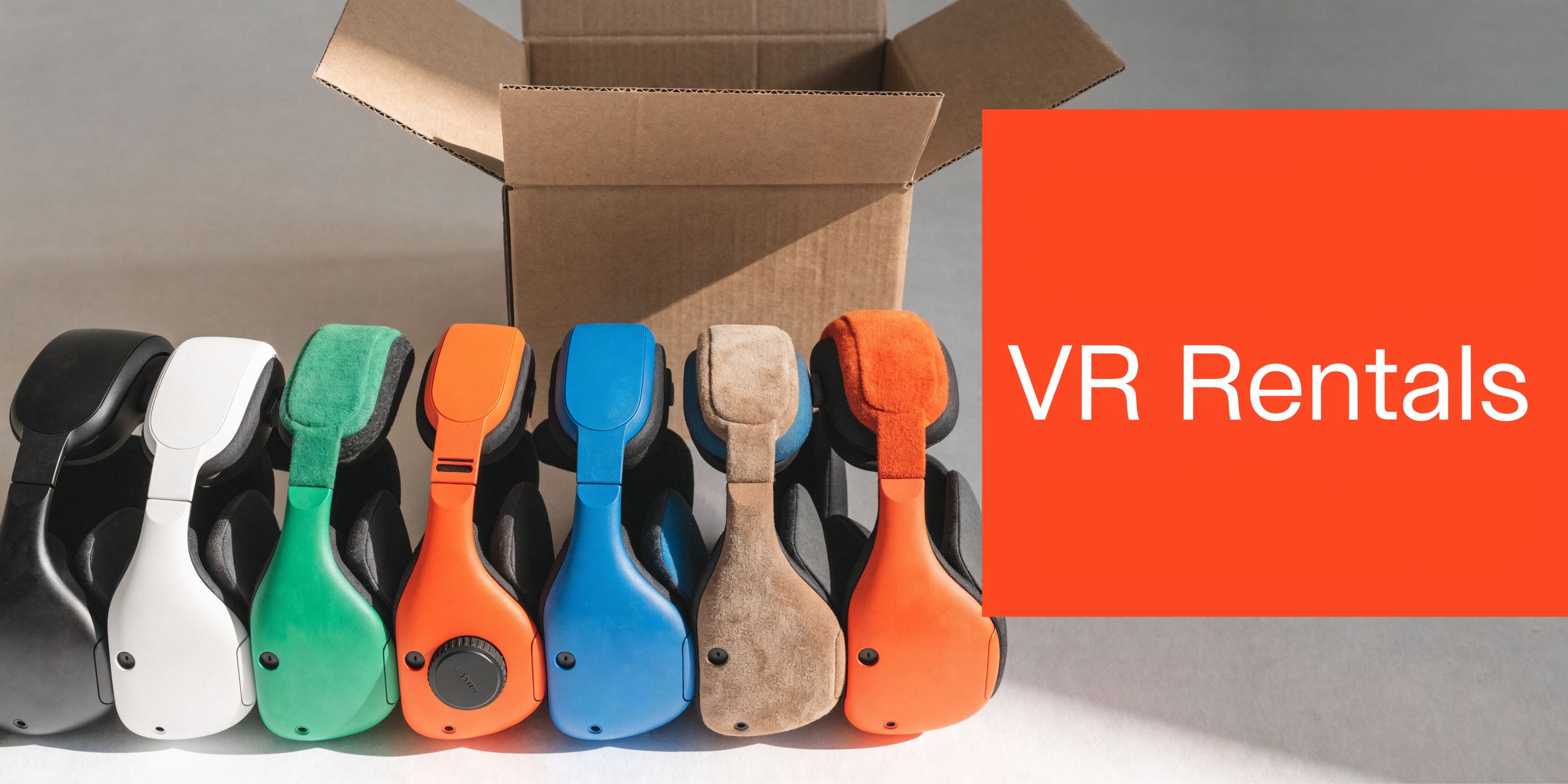 A line of colorful VR headsets arranged in front of an open cardboard shipping box for rentals.