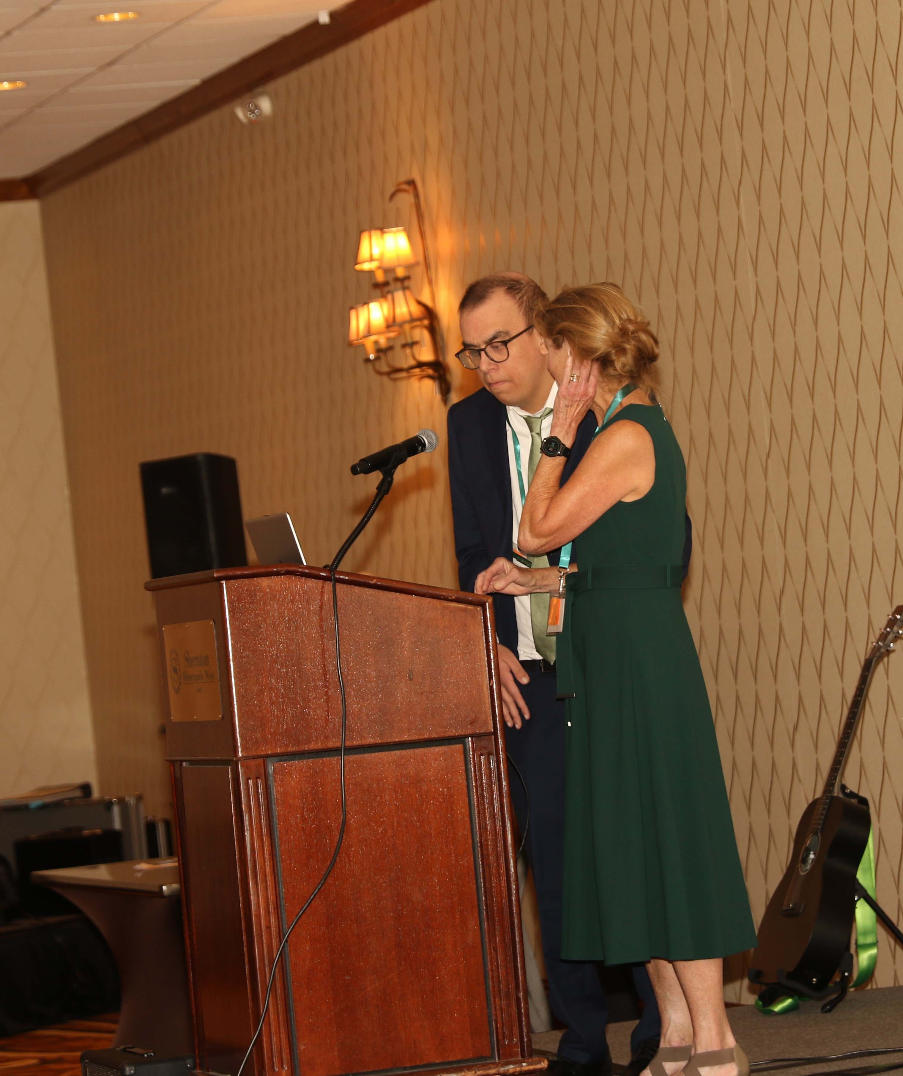 Photo of a man and woman standing on stage behind a podium.
