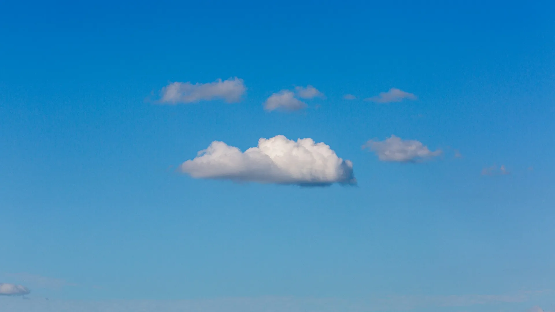 A single small white cloud drifting in an open blue sky