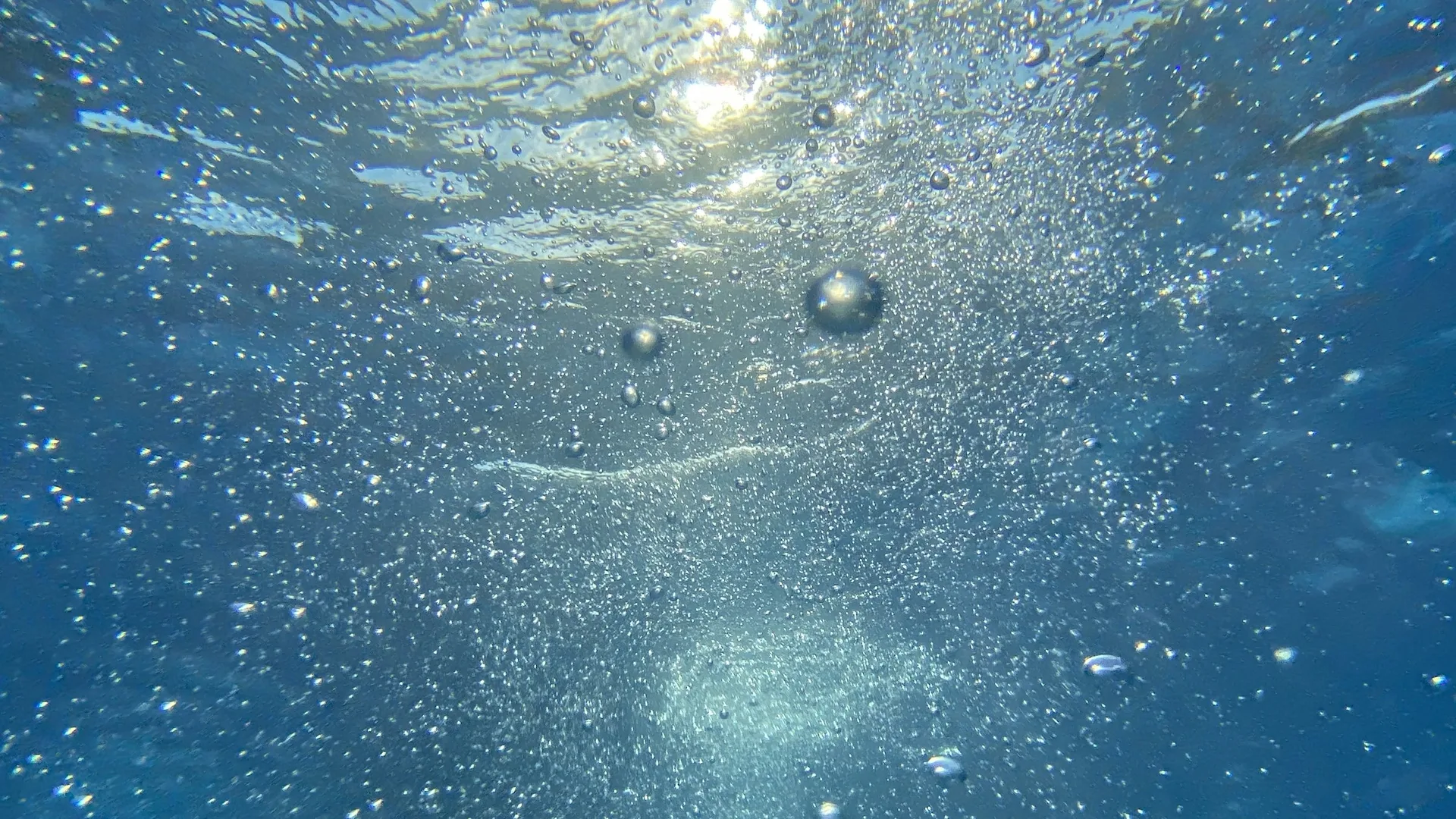 Sunlight breaking through the surface of clear blue water, with air bubbles rising
