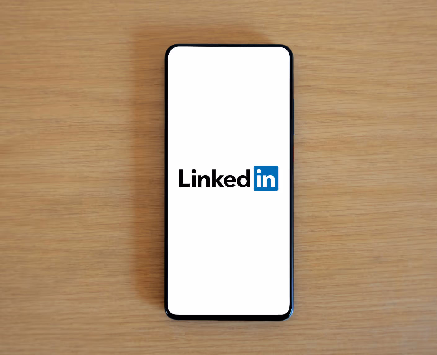 LinkedIn logo displayed on smartphone screen against wooden background