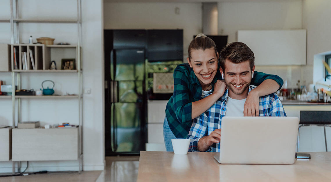 Samboerpar ser på laptop sammen på kjøkkenet