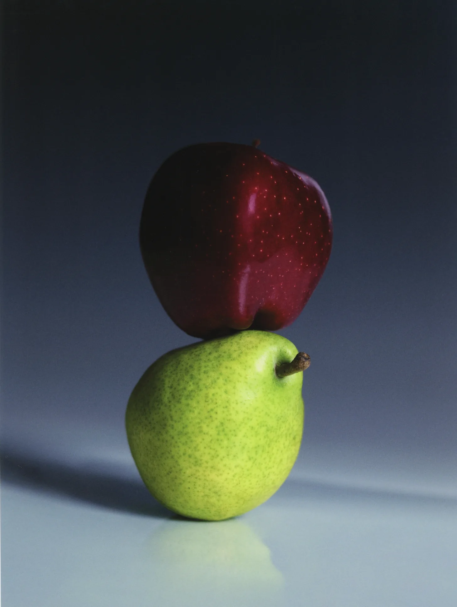 A red apple balanced on a green pear