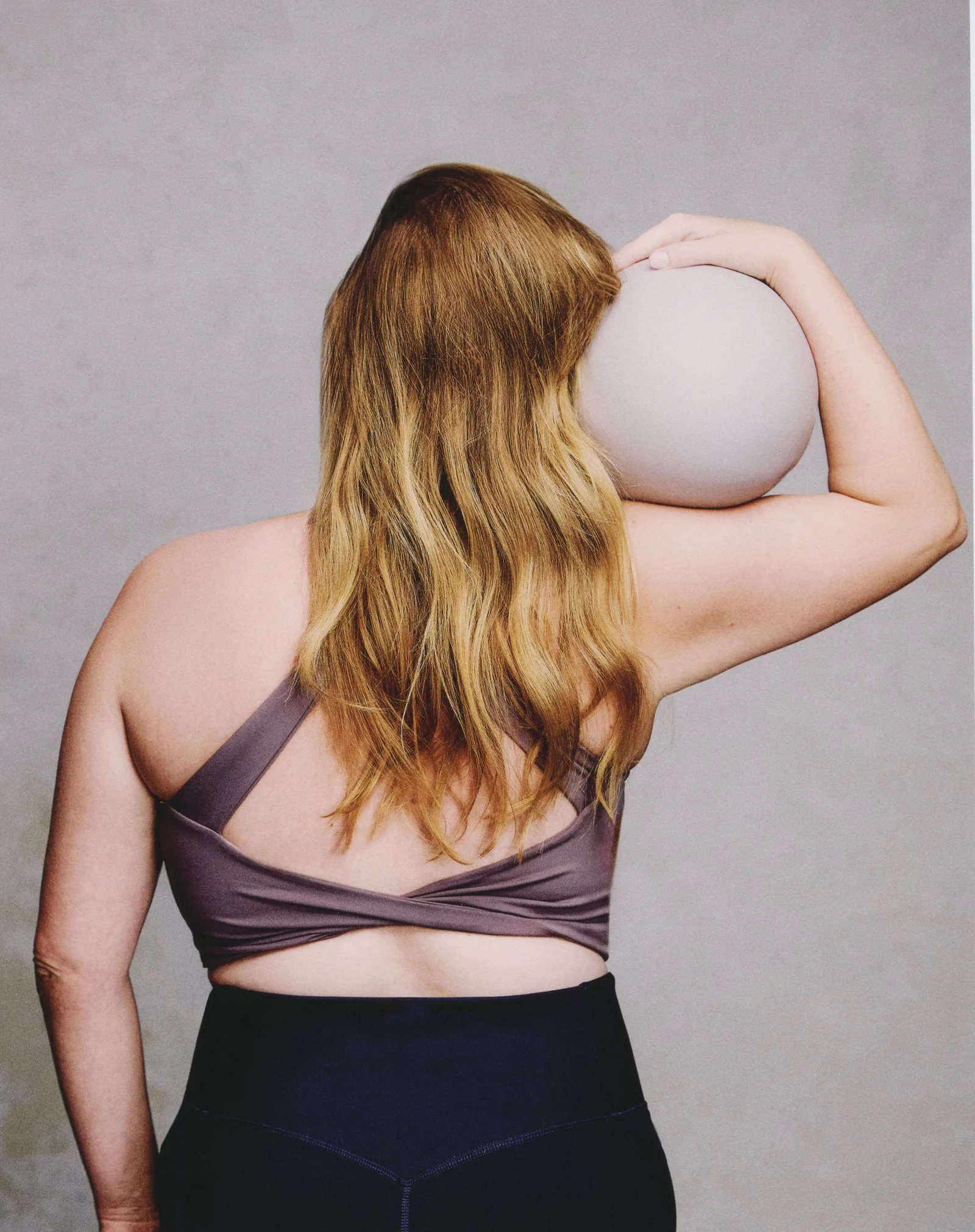 Woman seen from behind, resting an exercise ball on her shoulder