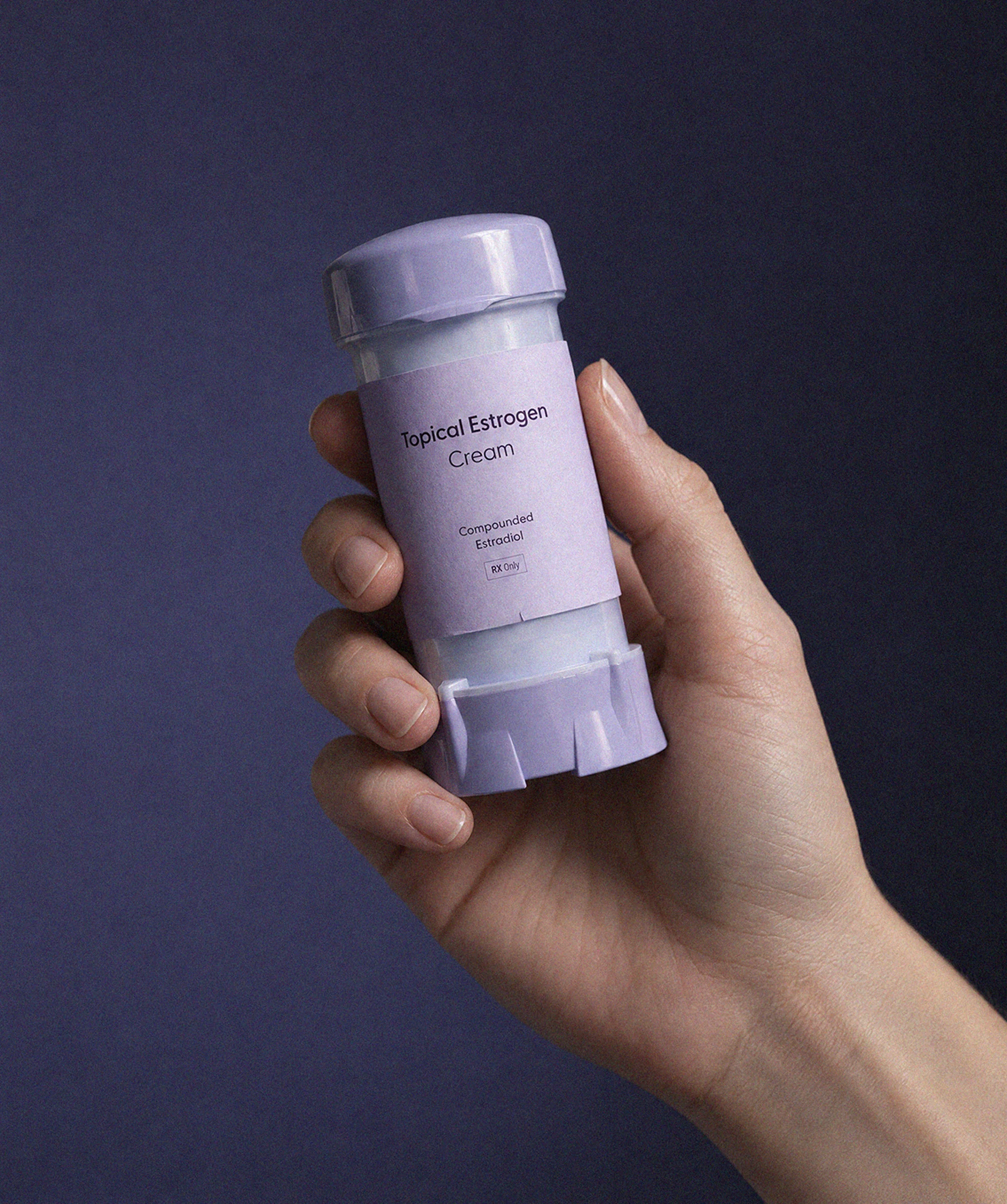 A hand holding Found topical estrogen cream, compounded estradiol, against a deep purple background