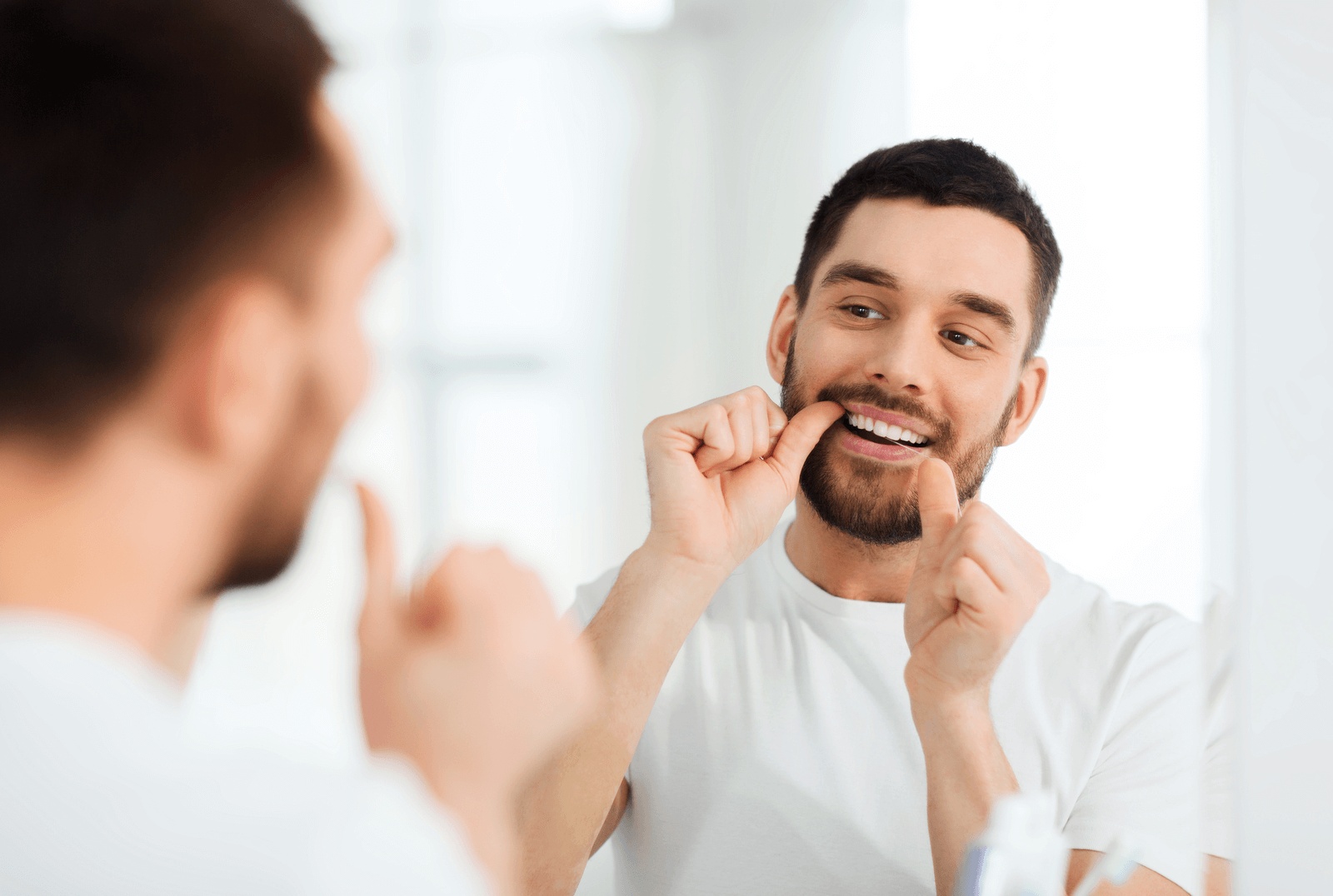 Man flossing his teeth in the bathroom mirror, demonstrating habits to prevent gingivitis and visiting the best dentist in Naperville, IL, for healthy gums.