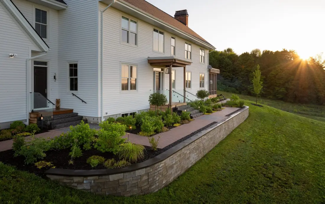 Stone retaining wall planter beside a white farmhouse