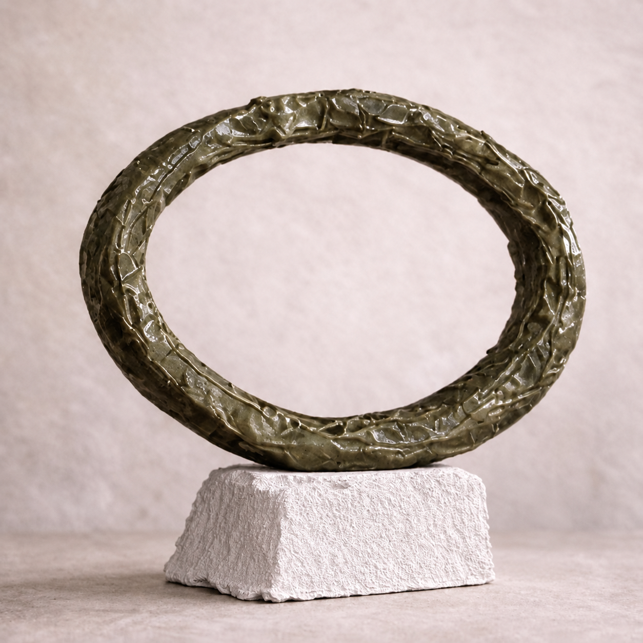 Continuum, olive-green circular sculpture on its textured pale pedestal