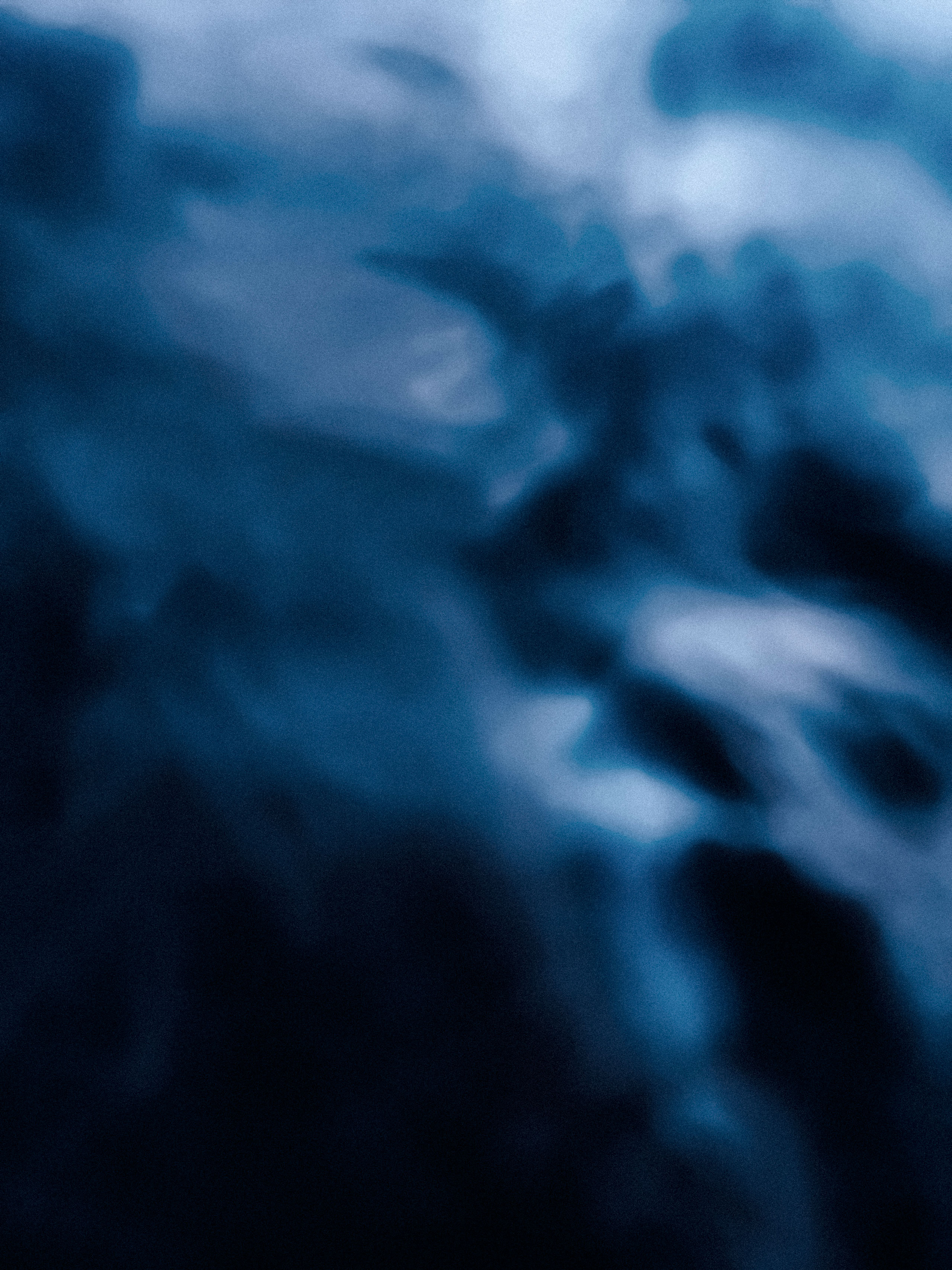 Abstract underwater image featuring swirling shades of dark blue and cyan, with soft, cloud-like formations and diffused lighting. The blurred textures and tonal gradients evoke a sense of depth and movement, resembling underwater currents or the surface distortion seen from below. The absence of distinct objects enhances the dreamy, immersive quality.