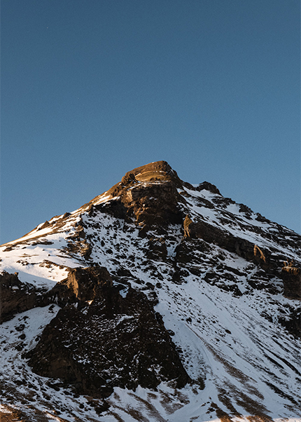 Snow-covered mountain peak in Iceland lit by warm sunset light against a clear blue sky.