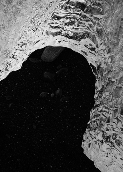 Black and white photo of an arch-shaped piece of glacial ice on black volcanic sand in Iceland.