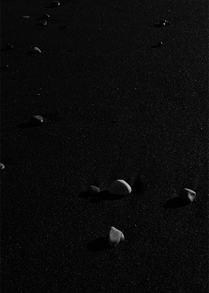 Minimalist black and white image of pebbles scattered across black volcanic sand in Iceland.