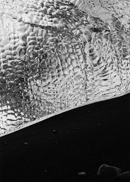 Black and white photo of textured glacial ice resting on black volcanic sand in Iceland.