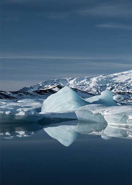 Blue icebergs floating in a glacier lagoon in Iceland with snowy mountains in the background and reflections in still water.