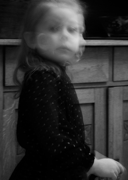Black and white photo of a blurred child turning toward the camera with a ghostlike face.