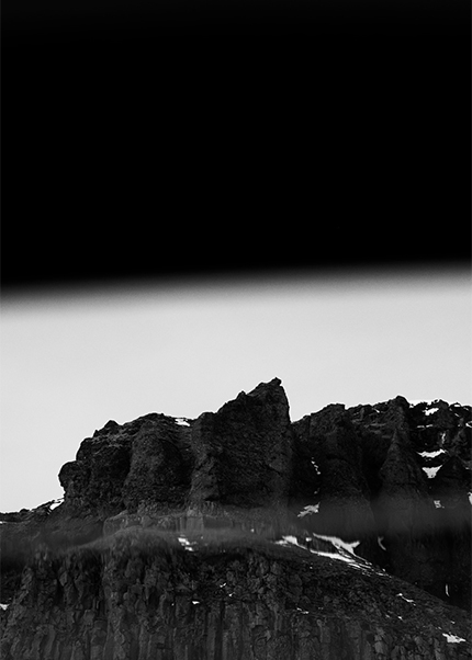 Black and white image of rugged volcanic cliffs in Iceland with patches of snow beneath a dark sky.