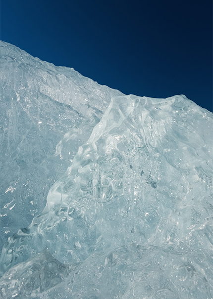 Sunlit glacial ice formation in Iceland with shimmering textures against a deep blue sky.