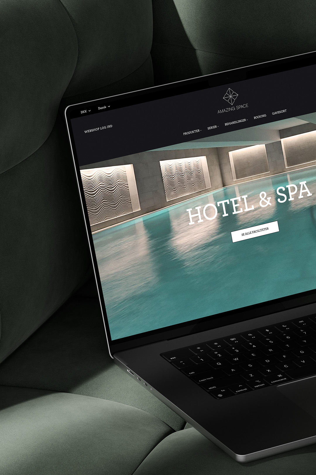 Close-up laptop mockup showcasing Amazing Space's website design with a modern indoor pool background, placed on a dark green cushioned surface.