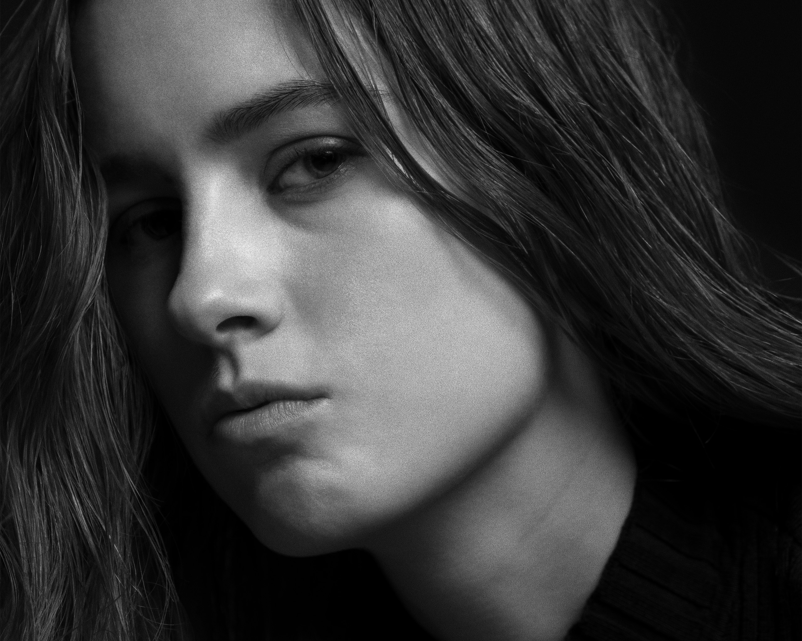 Black and white portrait photograph of Maria-May Brown with long hair, wearing a dark top, looking directly at the camera.