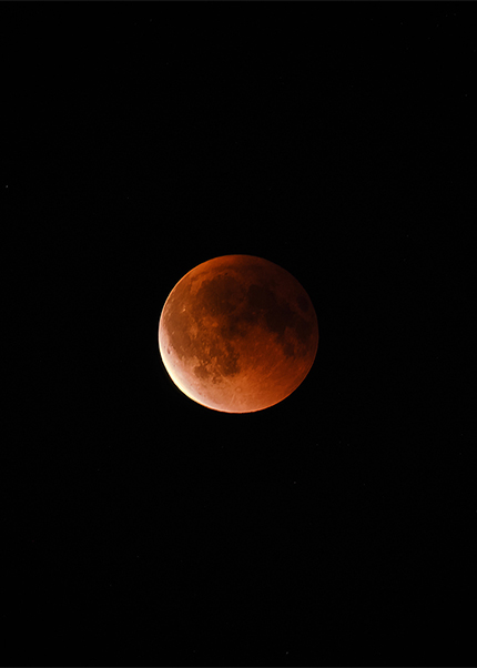 A reddish moon, photographed during a blood moon lunar eclipse, against a dark night sky over Copenhagen.