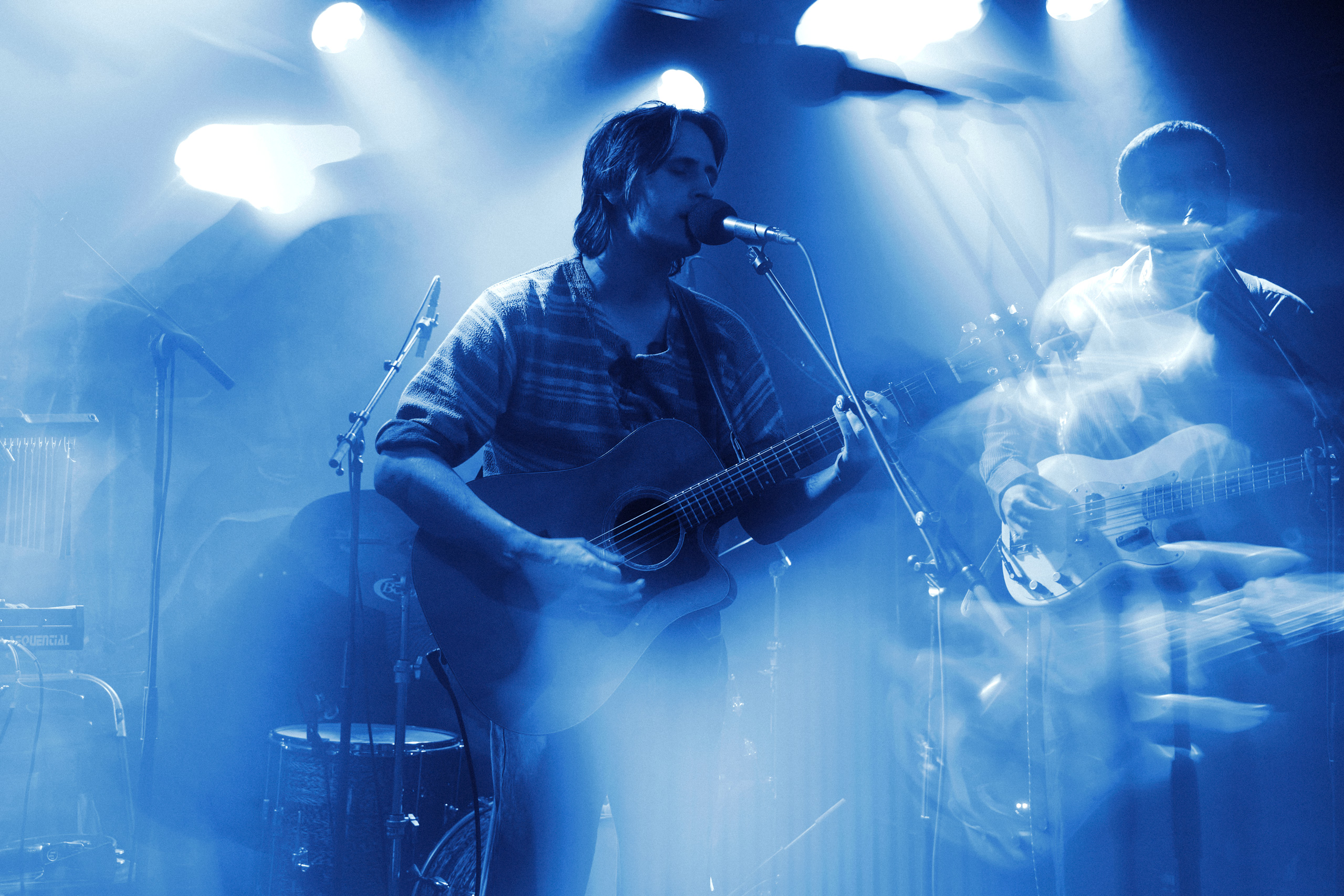 Wide shot of the band Thoughtfool performing at Rust, captured by Patrick Pankalla. The lead singer plays an acoustic guitar under blue stage lights.