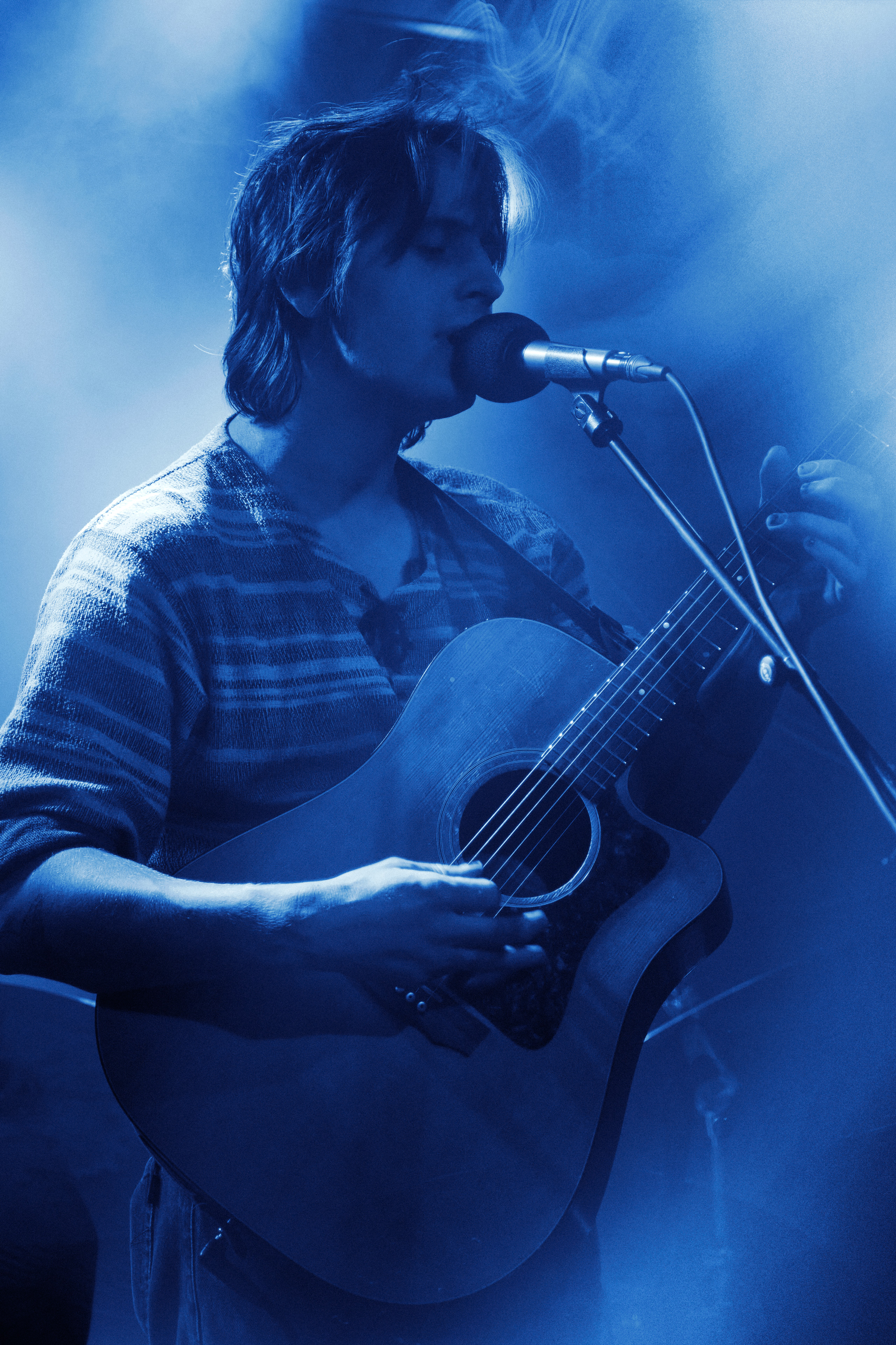 Patrick Pankalla's close-up blue-toned portrait of Thoughtfool's lead singer singing into a microphone while playing an acoustic guitar.