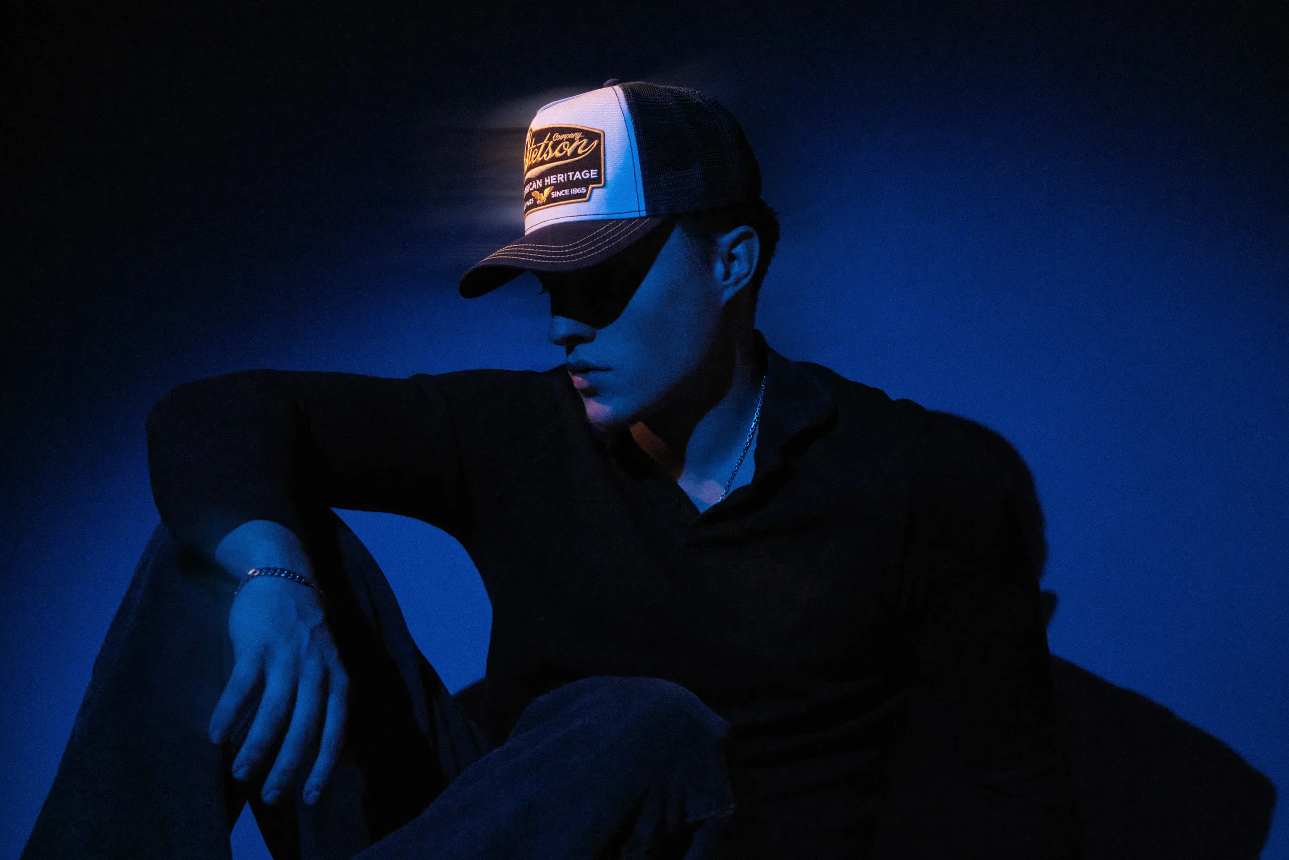 A widescreen desktop hero image of Asger looking down in a dark, blue-lit studio. Photography by Patrick Pankalla.