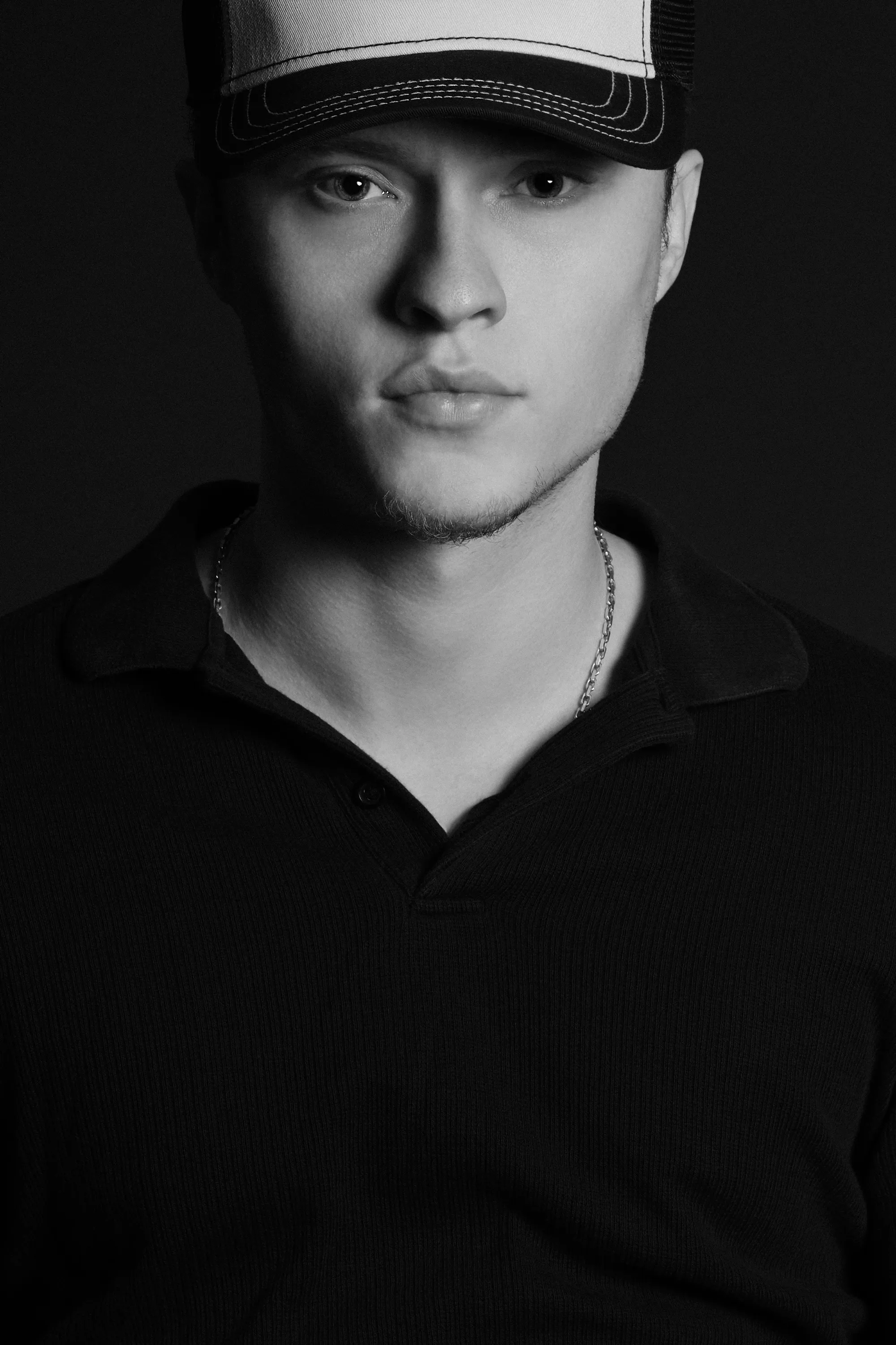 A black and white close-up portrait of Asger in a black polo shirt and cap, shot by Patrick Pankalla.
