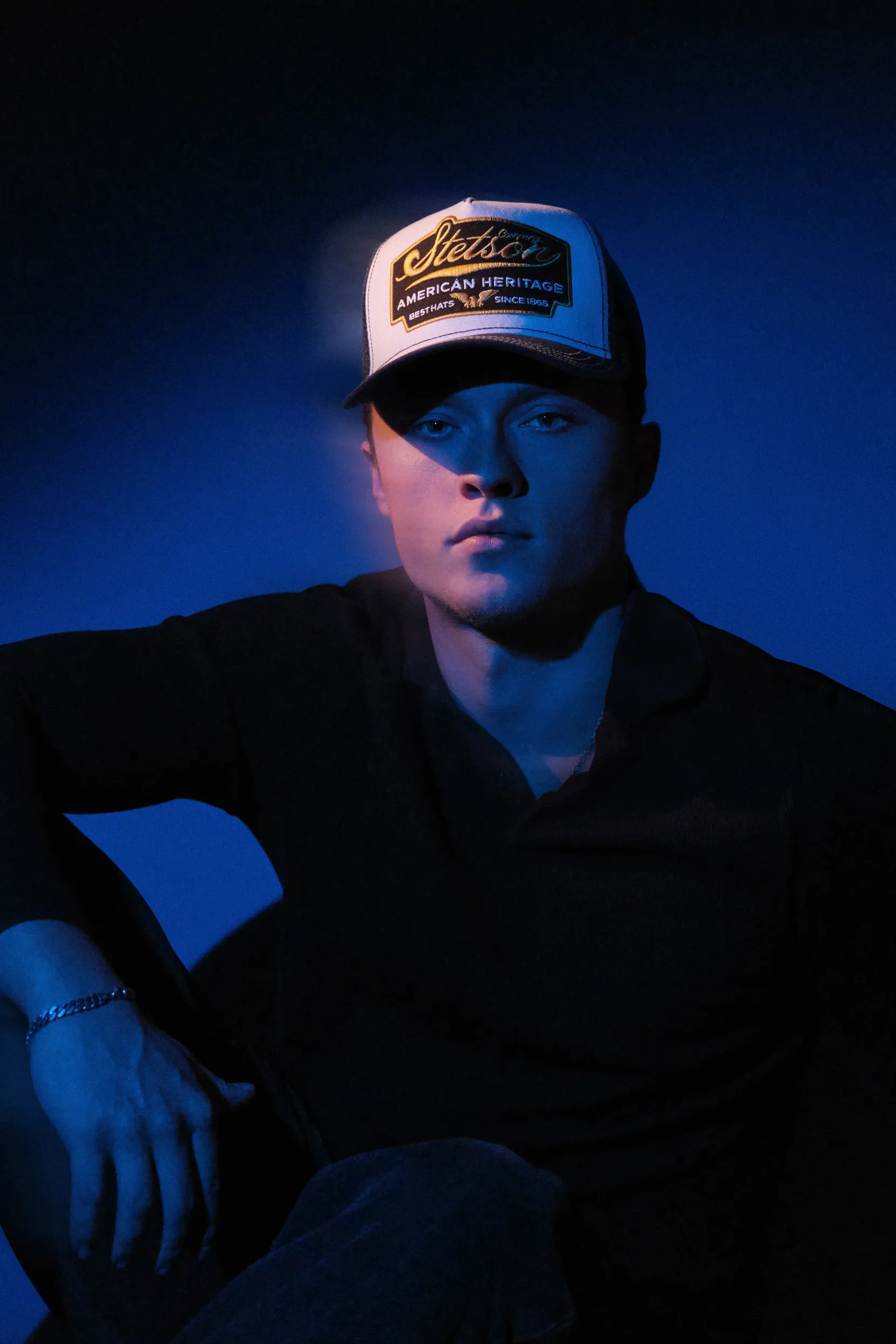 Patrick Pankalla's high-contrast studio portrait of Asger in a Stetson trucker hat under blue spotlights.
