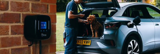 Photograph of an Ohme installation with the electric car being charge in the background, and a person taking their dog out of car boot.